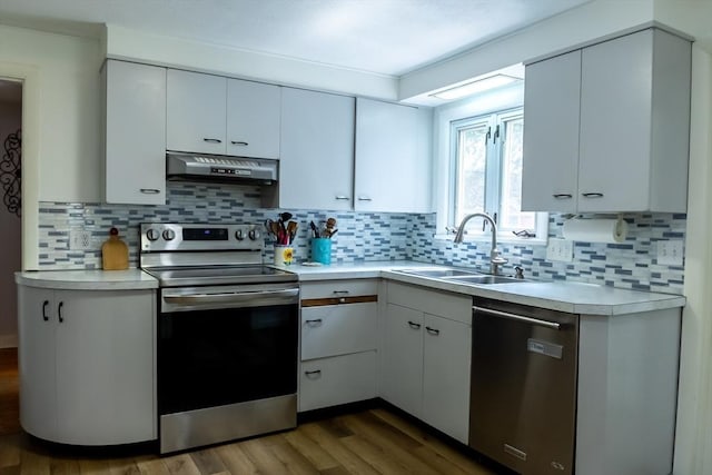 kitchen with stainless steel appliances, under cabinet range hood, a sink, light countertops, and wood finished floors