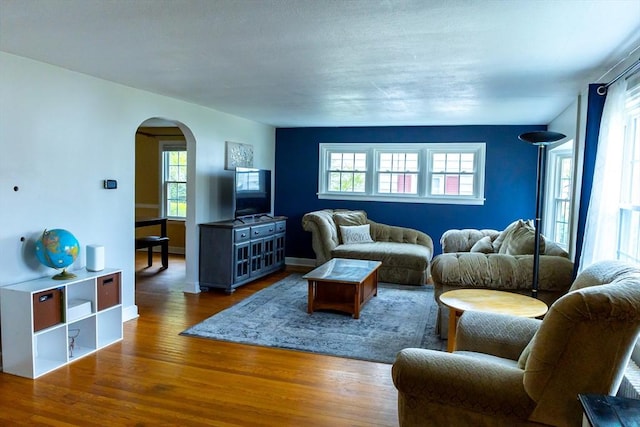 living area with arched walkways, wood finished floors, and healthy amount of natural light