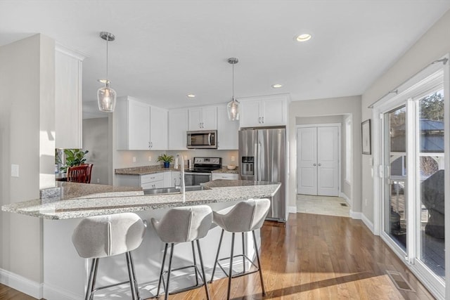 kitchen featuring appliances with stainless steel finishes, white cabinetry, a sink, wood finished floors, and a peninsula