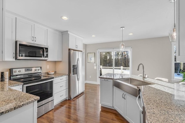 kitchen featuring light stone counters, dark wood-style flooring, white cabinets, appliances with stainless steel finishes, and decorative light fixtures