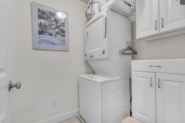 laundry area with stacked washer / dryer, cabinet space, and baseboards