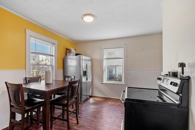 dining space featuring dark wood-style flooring, a wainscoted wall, and crown molding