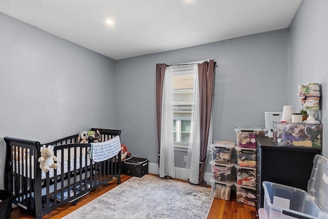 bedroom featuring recessed lighting, a nursery area, wood finished floors, and baseboards