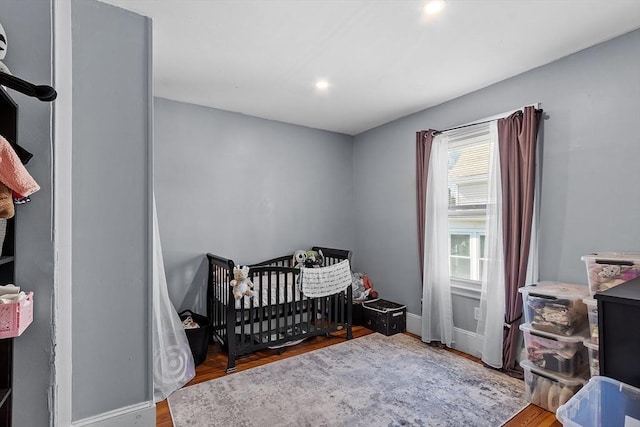 bedroom featuring recessed lighting, baseboards, wood finished floors, and a crib