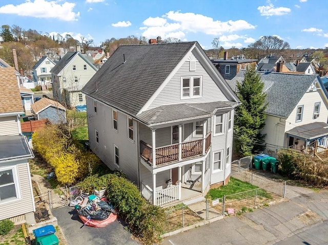 back of property with a gate, roof with shingles, a residential view, and a balcony