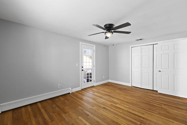 unfurnished bedroom featuring a closet, ceiling fan, a baseboard heating unit, and wood-type flooring