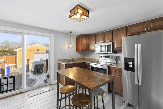 kitchen featuring sink, stainless steel appliances, hanging light fixtures, and light stone counters