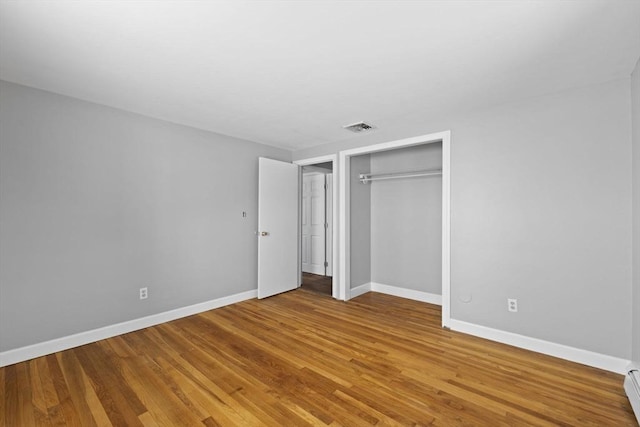 unfurnished bedroom with a closet, a baseboard radiator, and wood-type flooring