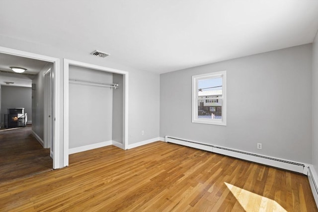 unfurnished bedroom featuring a closet, a baseboard radiator, and wood-type flooring