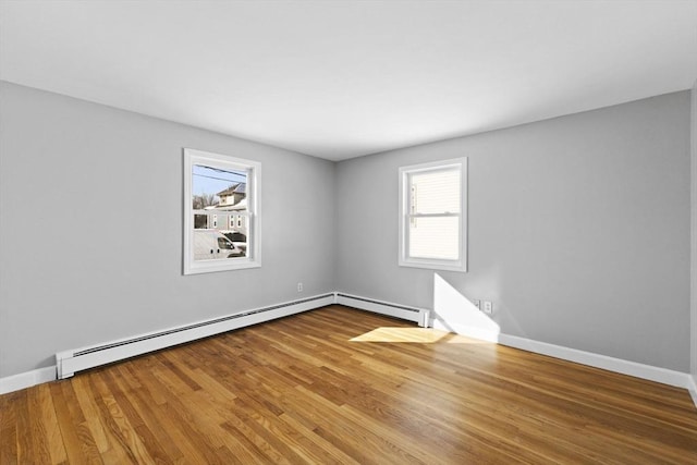 empty room featuring wood-type flooring, a wealth of natural light, and a baseboard heating unit