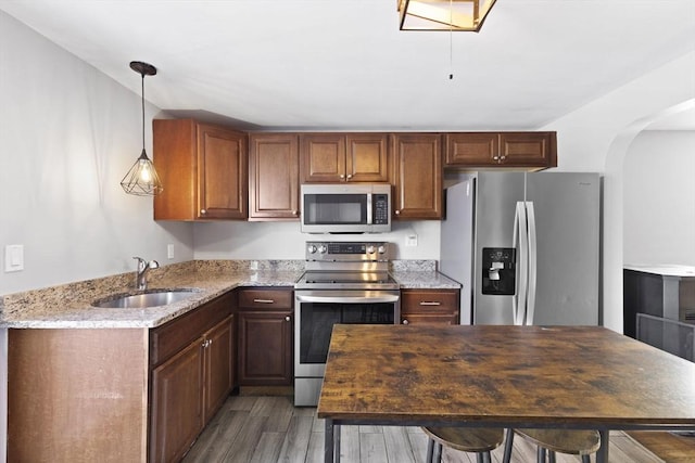 kitchen with hanging light fixtures, appliances with stainless steel finishes, sink, dark wood-type flooring, and light stone counters