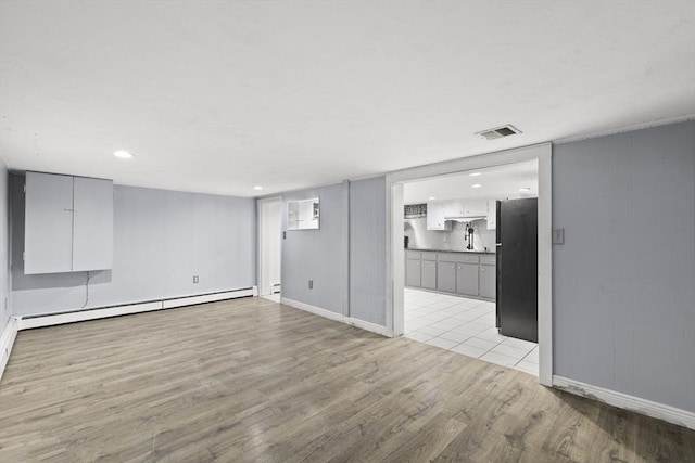 unfurnished living room featuring light hardwood / wood-style floors, a baseboard radiator, and sink