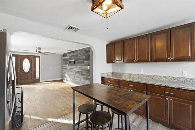 kitchen with light stone counters, dark brown cabinetry, stainless steel fridge, and light wood-type flooring