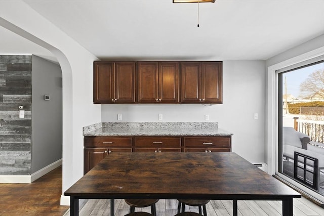 kitchen with dark brown cabinetry, a baseboard heating unit, light stone countertops, and dark wood-type flooring