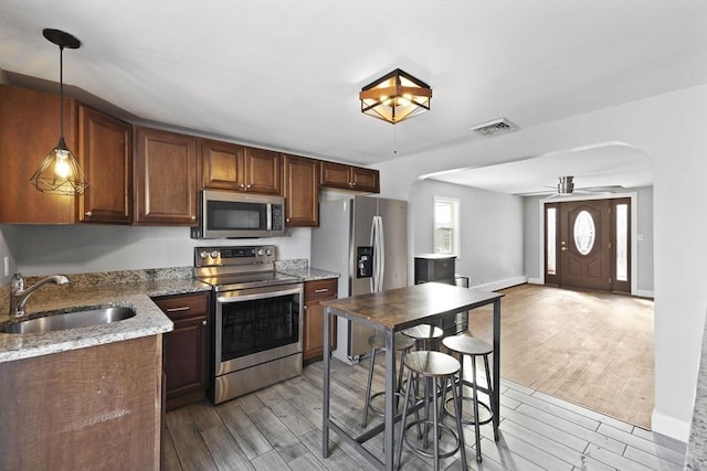 kitchen with light stone countertops, appliances with stainless steel finishes, sink, decorative light fixtures, and ceiling fan