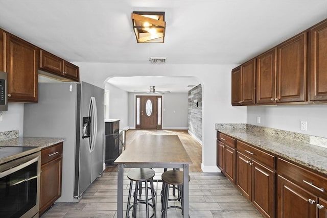 kitchen with light stone counters, a breakfast bar, appliances with stainless steel finishes, and ceiling fan