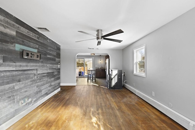 interior space with ceiling fan, wood walls, a baseboard heating unit, and dark hardwood / wood-style flooring