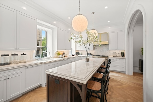 kitchen with a kitchen island, light stone counters, light parquet flooring, crown molding, and white cabinetry