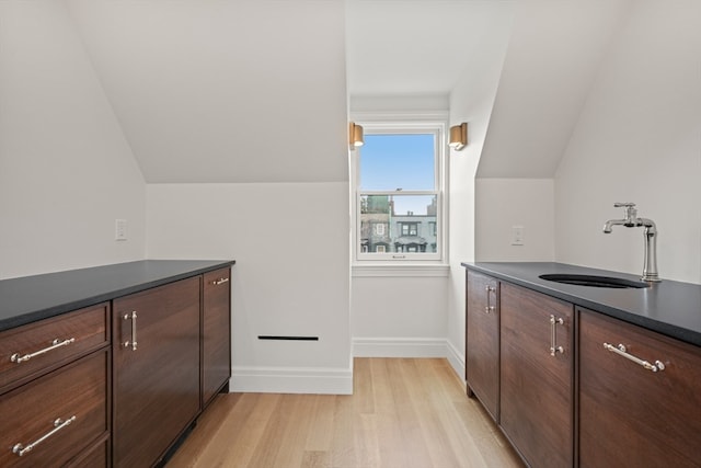 kitchen featuring vaulted ceiling, sink, light wood-type flooring, and dark brown cabinets