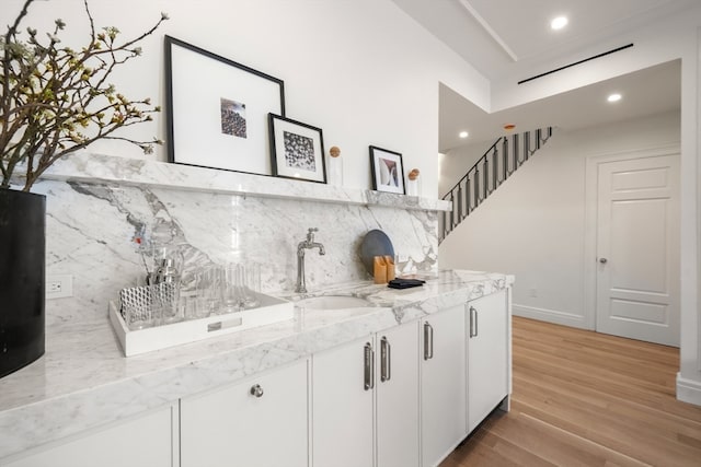 bar featuring white cabinets, sink, light hardwood / wood-style flooring, backsplash, and light stone countertops