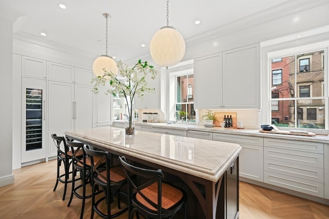 kitchen featuring pendant lighting, light parquet flooring, a kitchen island, white cabinetry, and light stone countertops