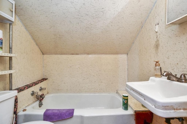 bathroom featuring a washtub, toilet, sink, and vaulted ceiling