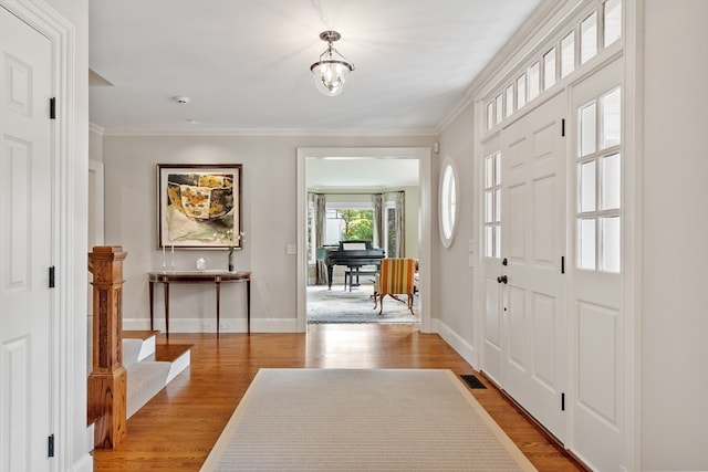 entryway featuring ornamental molding, light wood-type flooring, and a notable chandelier