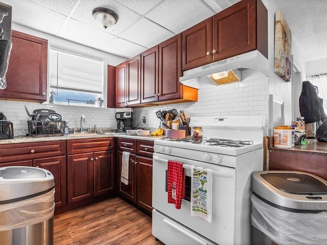 kitchen featuring dark brown cabinets, white range with gas stovetop, under cabinet range hood, a sink, and dark wood finished floors
