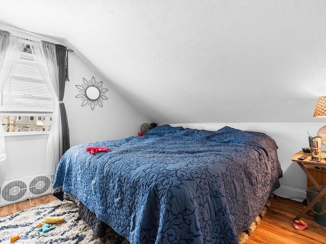bedroom with a textured ceiling, wood finished floors, and lofted ceiling