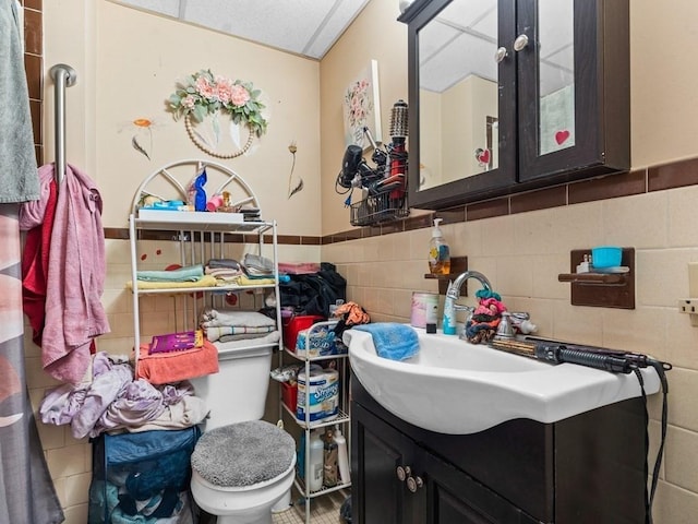 bathroom with wainscoting, tile walls, vanity, and toilet