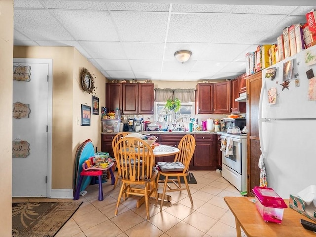 kitchen with light tile patterned floors, white appliances, a sink, and a paneled ceiling