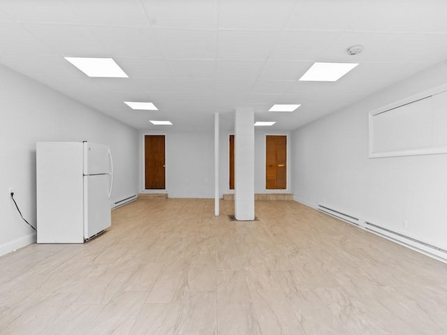 below grade area featuring baseboard heating, baseboards, freestanding refrigerator, and a drop ceiling
