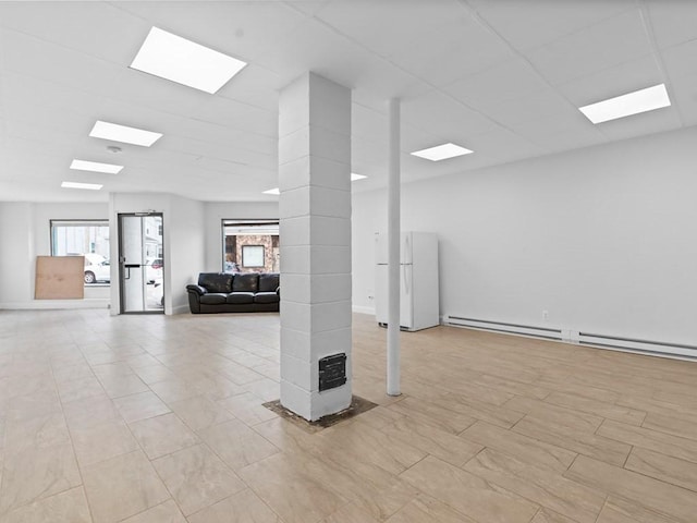 below grade area with freestanding refrigerator and a baseboard radiator