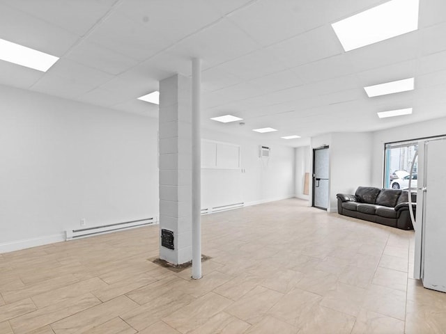 basement featuring baseboards, freestanding refrigerator, a wall unit AC, and baseboard heating
