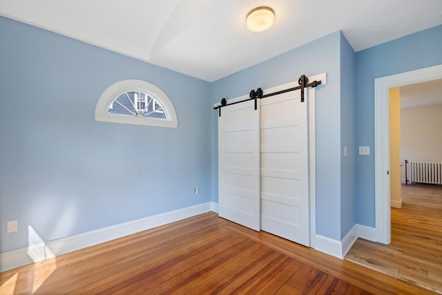 124 Boston Ave, Medford, MA 02155 - unfurnished bedroom with radiator, a barn door, hardwood / wood-style flooring, and baseboards