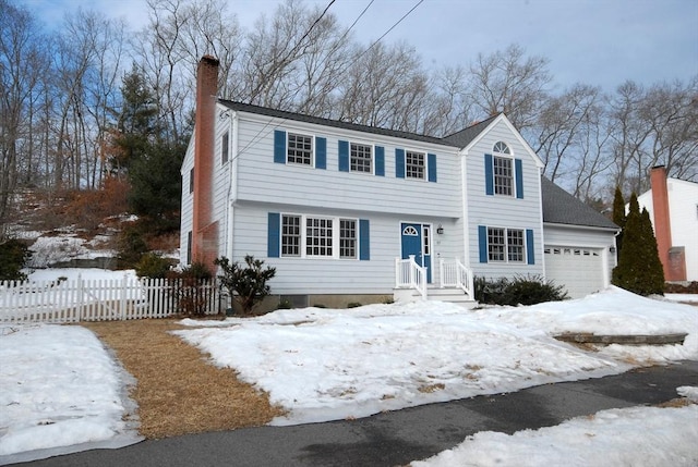 colonial house with an attached garage, a chimney, and fence