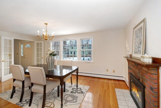 dining area with a fireplace, french doors, an inviting chandelier, light wood-style floors, and a baseboard radiator