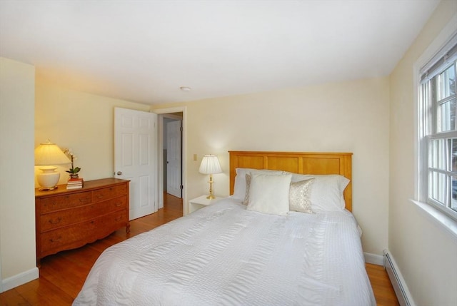 bedroom featuring a baseboard heating unit, baseboards, and wood finished floors