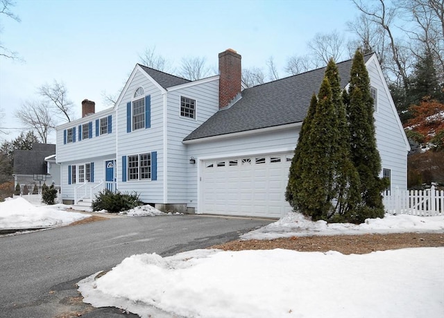 view of front facade featuring driveway, fence, roof with shingles, an attached garage, and a chimney