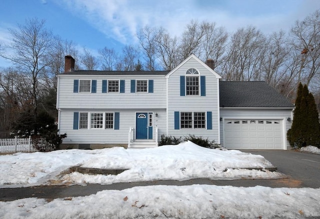 colonial inspired home with an attached garage, a chimney, driveway, and fence