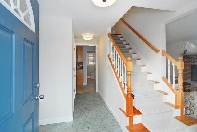 tiled entrance foyer featuring stairway, a brick fireplace, and baseboards