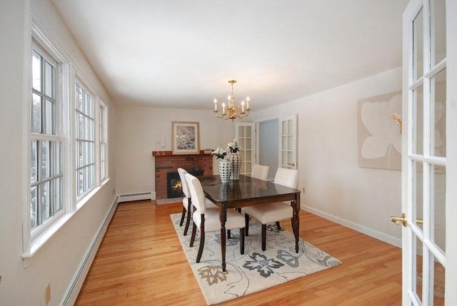 dining space featuring a baseboard heating unit, french doors, light wood finished floors, baseboards, and a brick fireplace