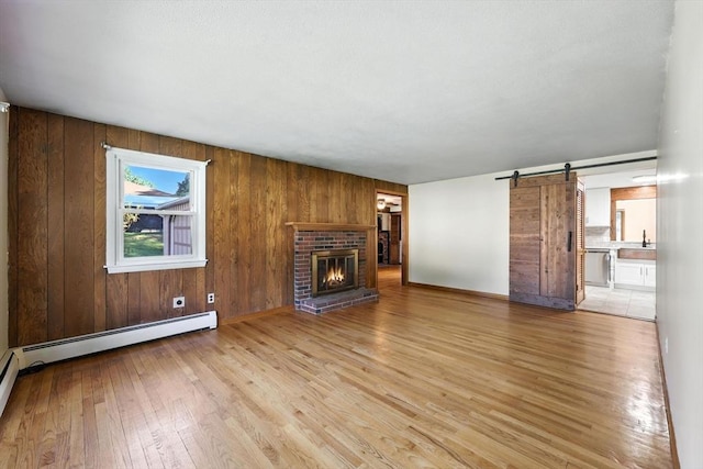51 Glenview Dr, West Springfield, MA 01089 - unfurnished living room featuring light wood-type flooring, a barn door, a fireplace, baseboard heating, and wooden walls