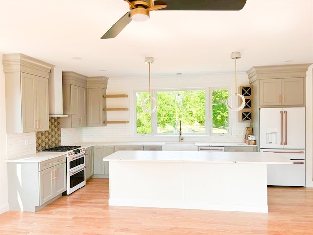 kitchen featuring white appliances, wall chimney range hood, light wood-type flooring, a kitchen island, and hanging light fixtures