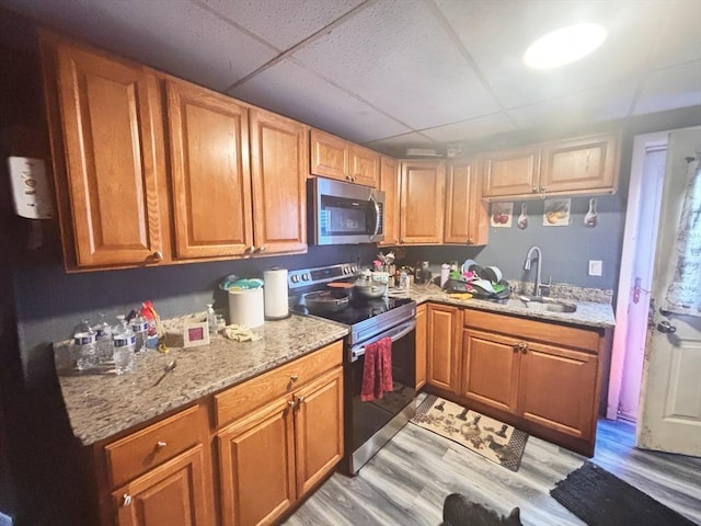 kitchen featuring light stone counters, a paneled ceiling, stainless steel appliances, a sink, and light wood-style floors