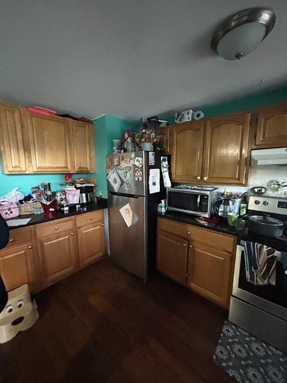 kitchen featuring dark countertops, under cabinet range hood, stainless steel appliances, and dark wood-type flooring