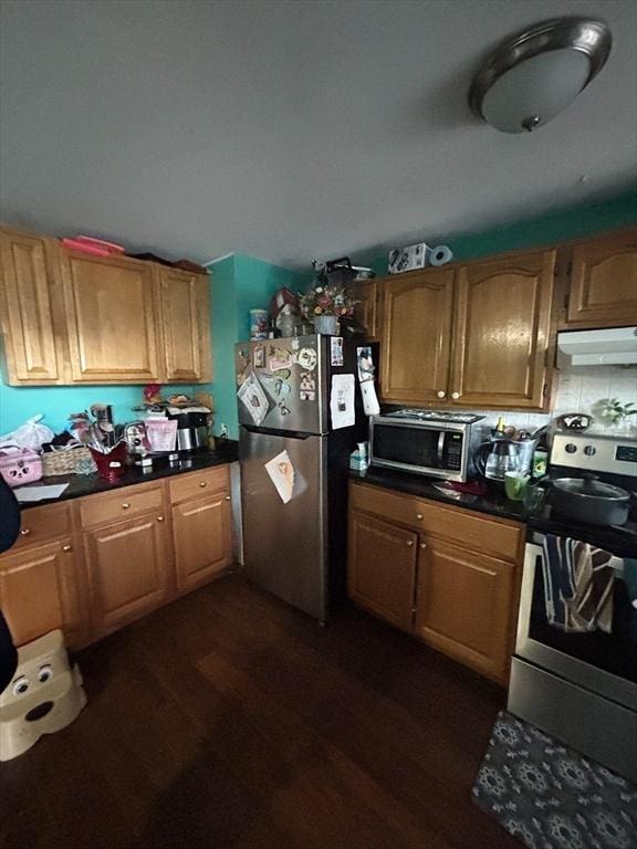 kitchen featuring stainless steel appliances, dark countertops, dark wood finished floors, and under cabinet range hood