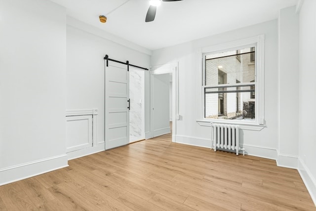 spare room featuring light wood-type flooring, radiator heating unit, a barn door, and ceiling fan