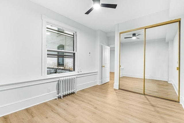 unfurnished bedroom featuring light wood-type flooring, ceiling fan, radiator heating unit, and a closet