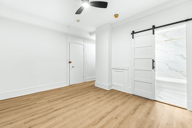 spare room featuring light wood-type flooring, a barn door, and ceiling fan